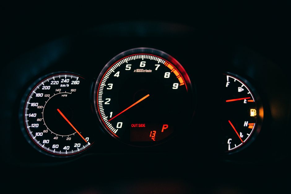 A car instrument cluster photographed close up, showing a tachometer between a speedometer and a fuel gauge, with white needles and scales on a dark ground.