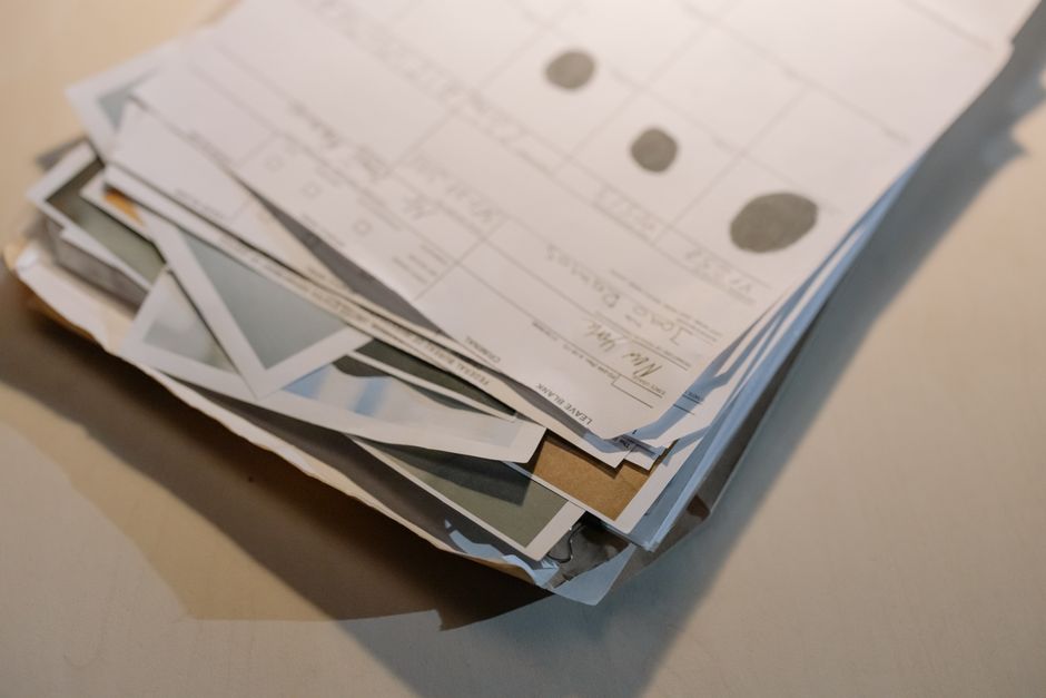 A close-up of a thick stack of assorted printed papers and documents resting on a desk surface.