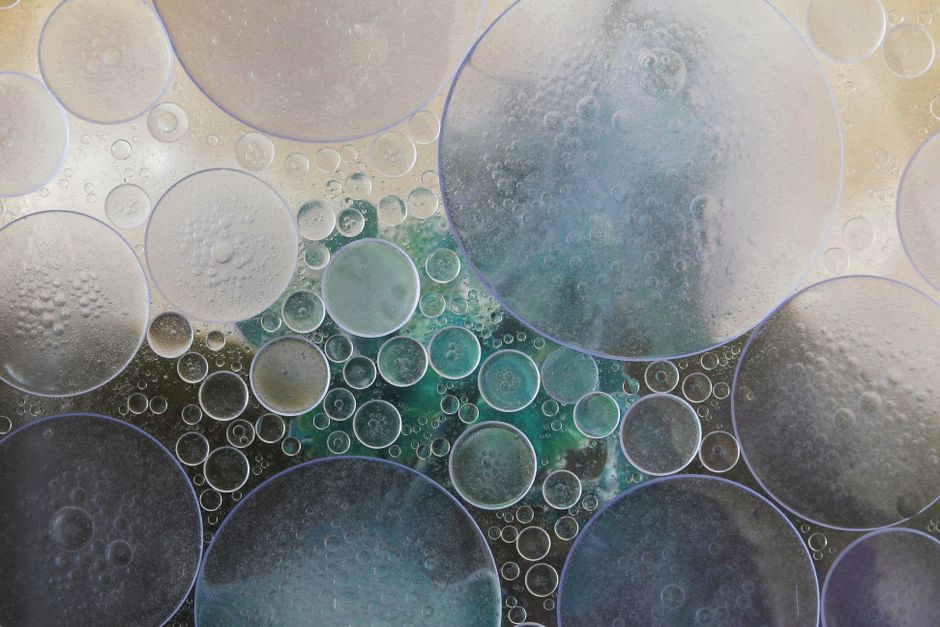 A macro photograph of soap bubbles of different sizes pressed together in liquid, their edges meeting and overlapping.