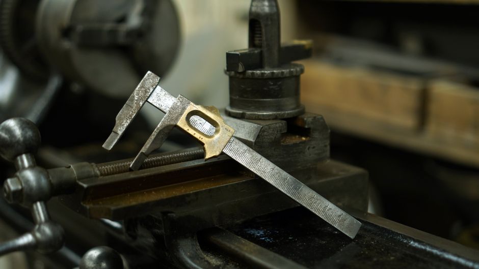 A close-up of a metal vernier caliper resting on industrial machinery in a workshop.
