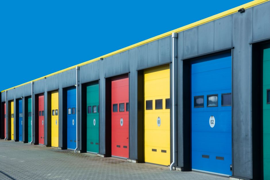 A row of industrial garage doors photographed straight on, each painted a different colour: blue, red, yellow and green.