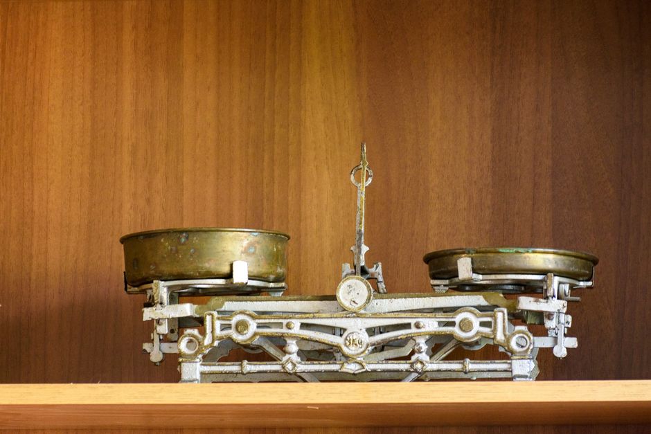 A vintage brass balance scale with two pans, standing on a wooden kitchen shelf.