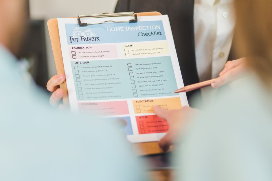 Close-up of two hands holding a clipboard with a printed home inspection checklist on it.