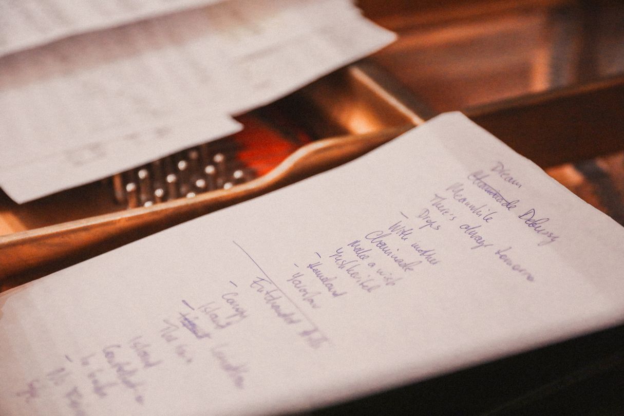 A handwritten checklist on a sheet of plain paper resting on a desk in warm light, with several items already ticked off.