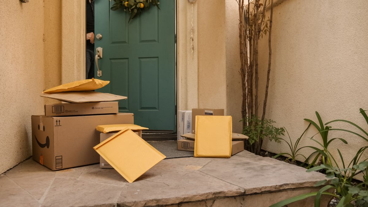 Several delivery packages and cardboard parcels stacked on the porch of a teal front door.