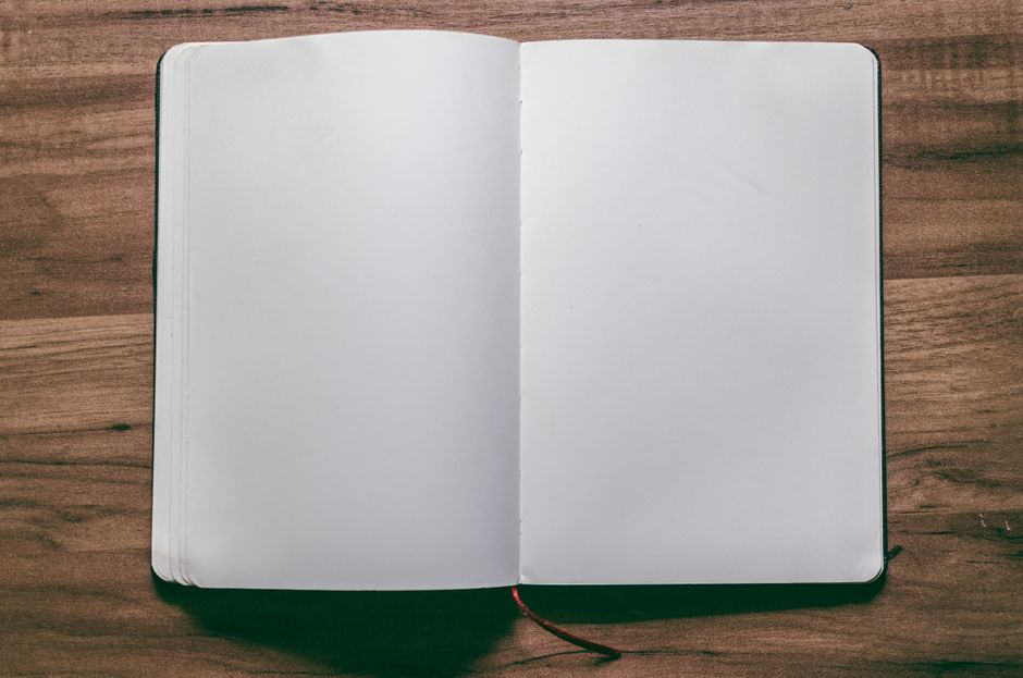A top-down view of an open blank notebook on a wooden desk beside a pen.