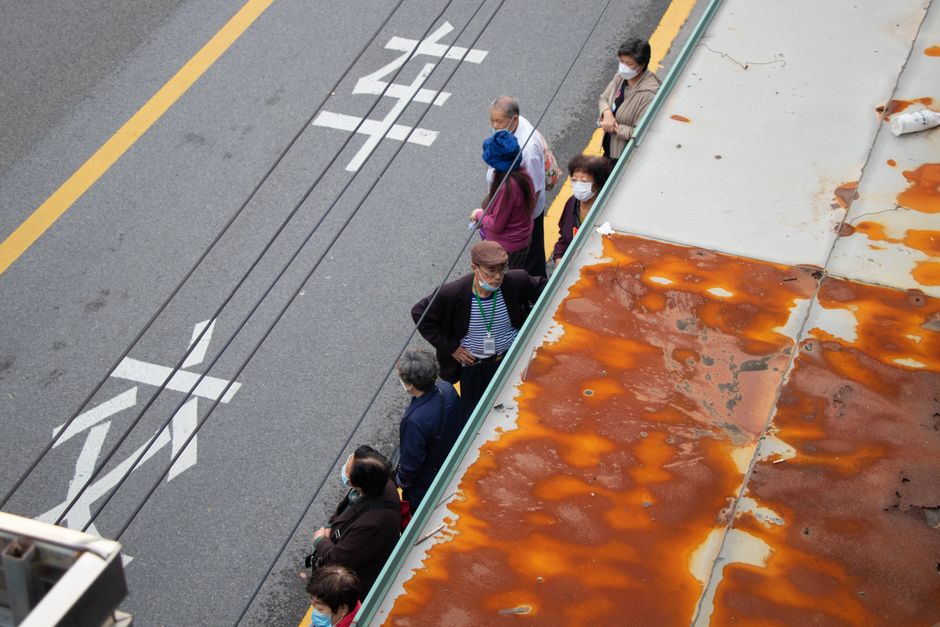 A high angle view of people standing in a queue at a bus stop on a street.