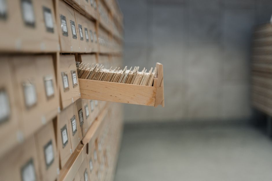 A wall mounted wooden card catalogue in an archive, its long narrow drawers each fitted with a brass label holder.