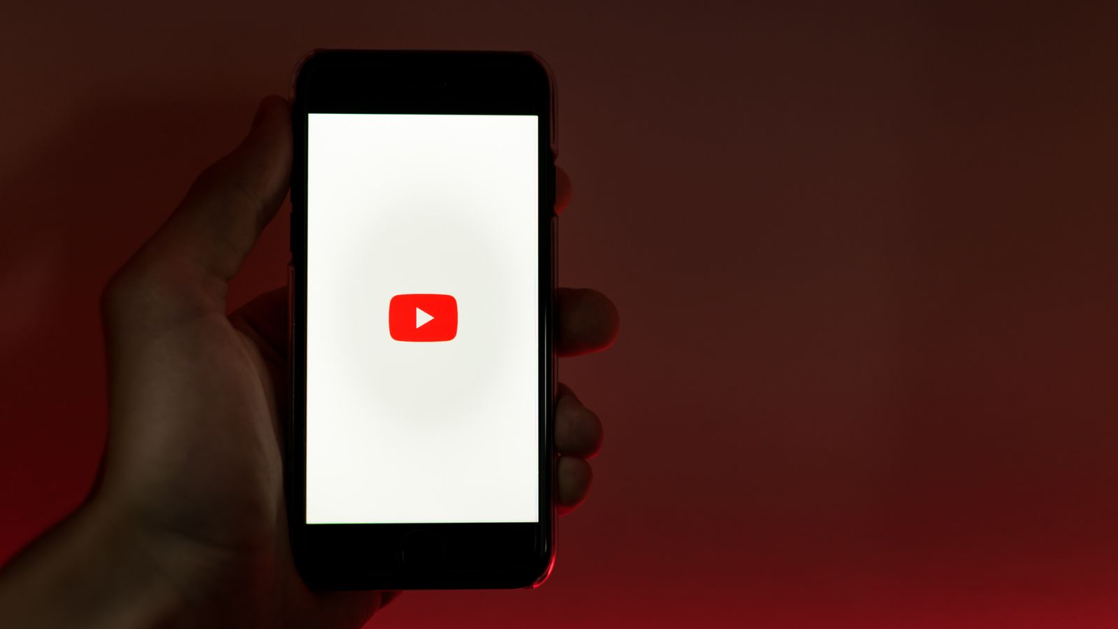A hand holding a smartphone with the YouTube app open, against a red background.