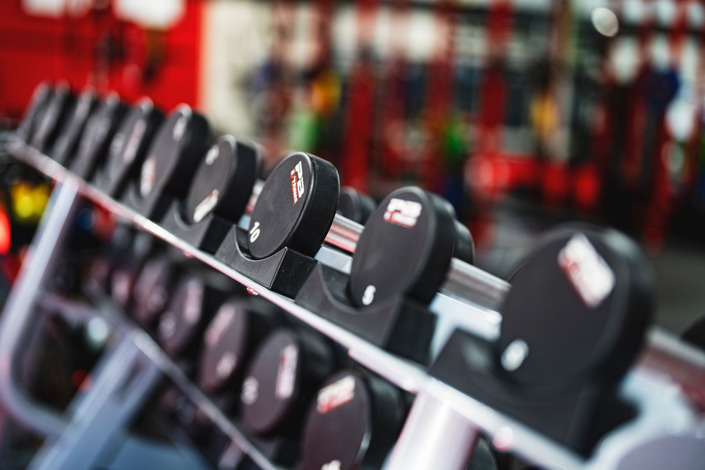 A row of dumbbells racked in order of weight in a gym, shot close and low with the room out of focus behind.