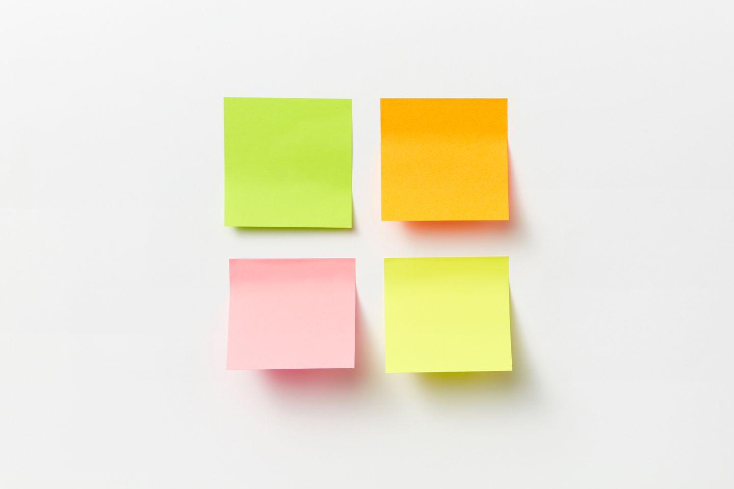 Four sticky notes in different colours stuck at slight angles on a plain white wall.