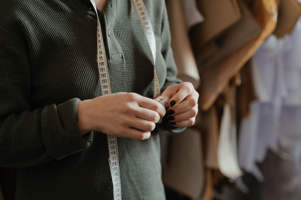 Close-up of a person using a measuring tape over patterned fabric in a sewing studio, marking a measurement before cutting.