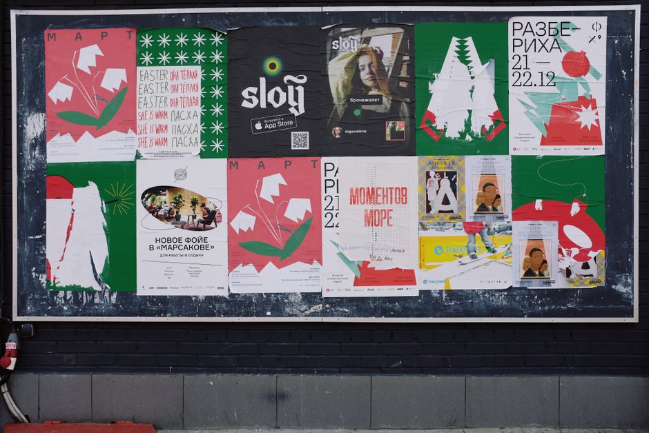 A black wall densely covered in overlapping colourful printed posters and flyers, layered on top of each other.
