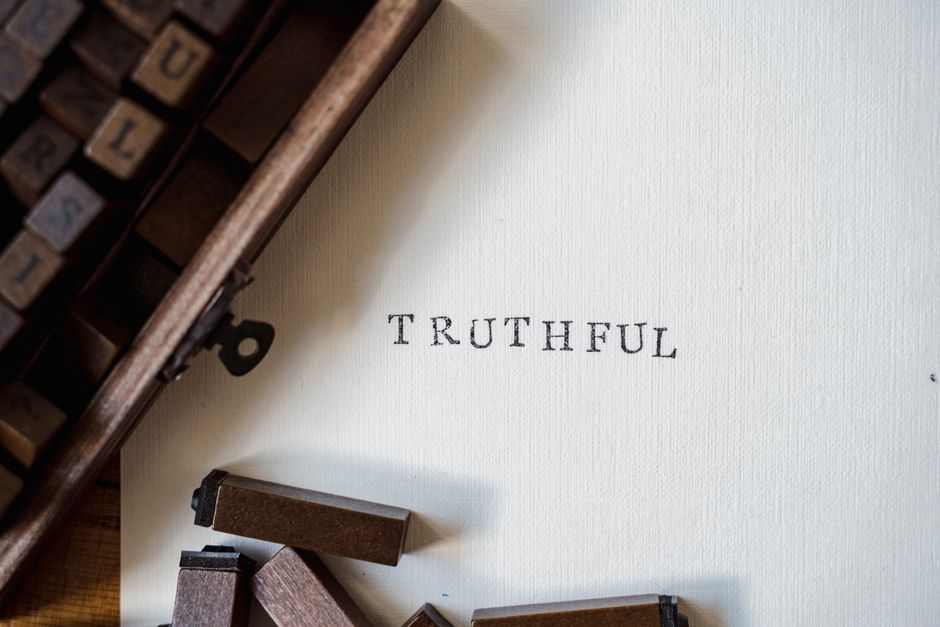 Wooden letterpress blocks, most still racked in a tray and a few lying loose, beside textured paper printed with the single word TRUTHFUL.