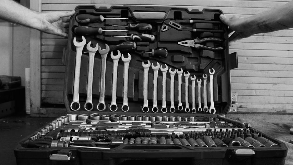 An open toolbox photographed from above in black and white, spanners and sockets of every size laid out in rows.