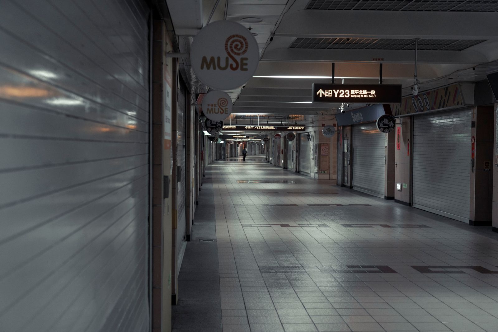 A long underground pedestrian passageway lined with signage and strip lighting, with a single figure walking away in the far distance.