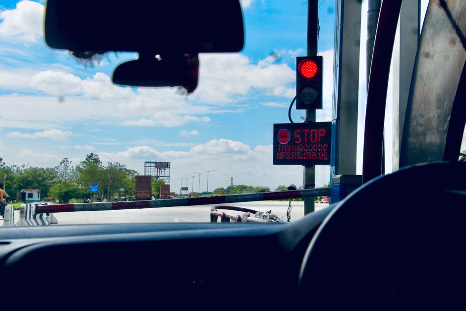The view from inside a car at a toll booth, with a red stop signal and a raised barrier ahead.