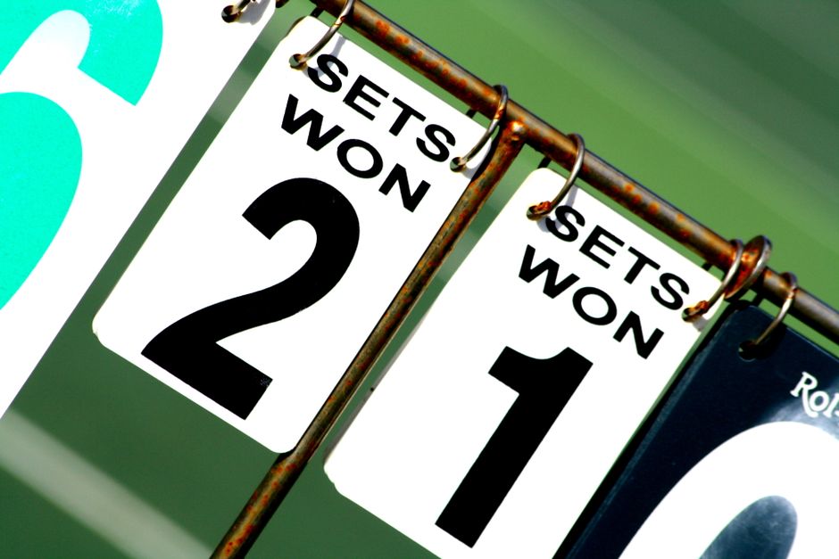 A close-up of a tennis scoreboard with sliding number panels showing sets won by each player.