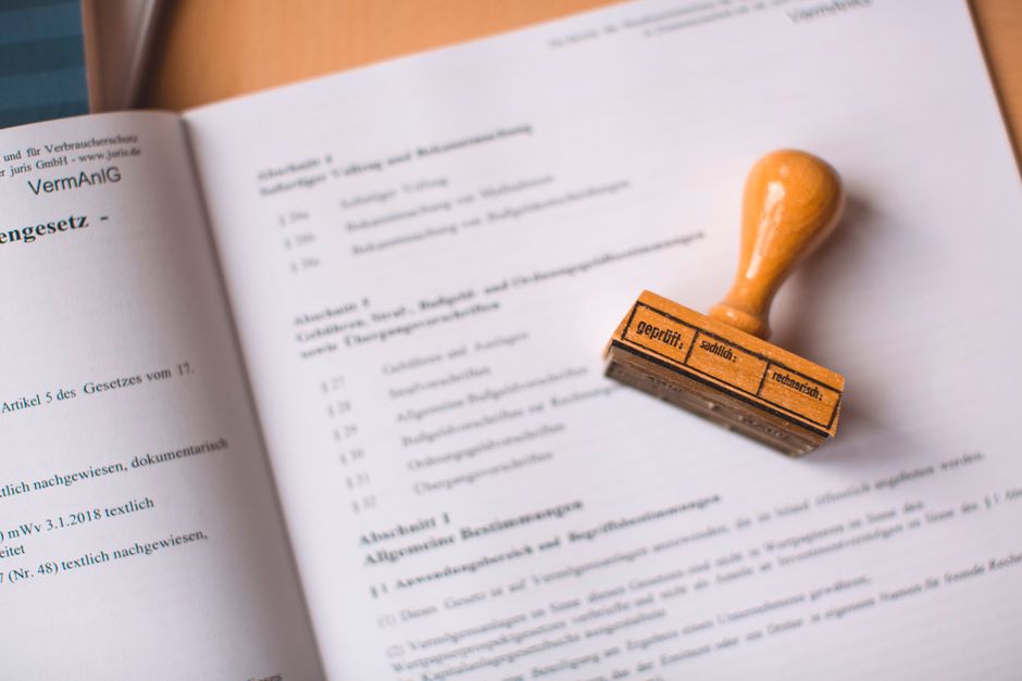 A close-up of a wooden handled rubber stamp resting on an open printed document on a desk.