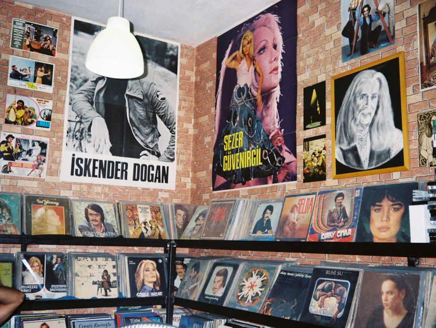 A wall of a record shop covered edge to edge in overlapping music posters and album covers in many colours.